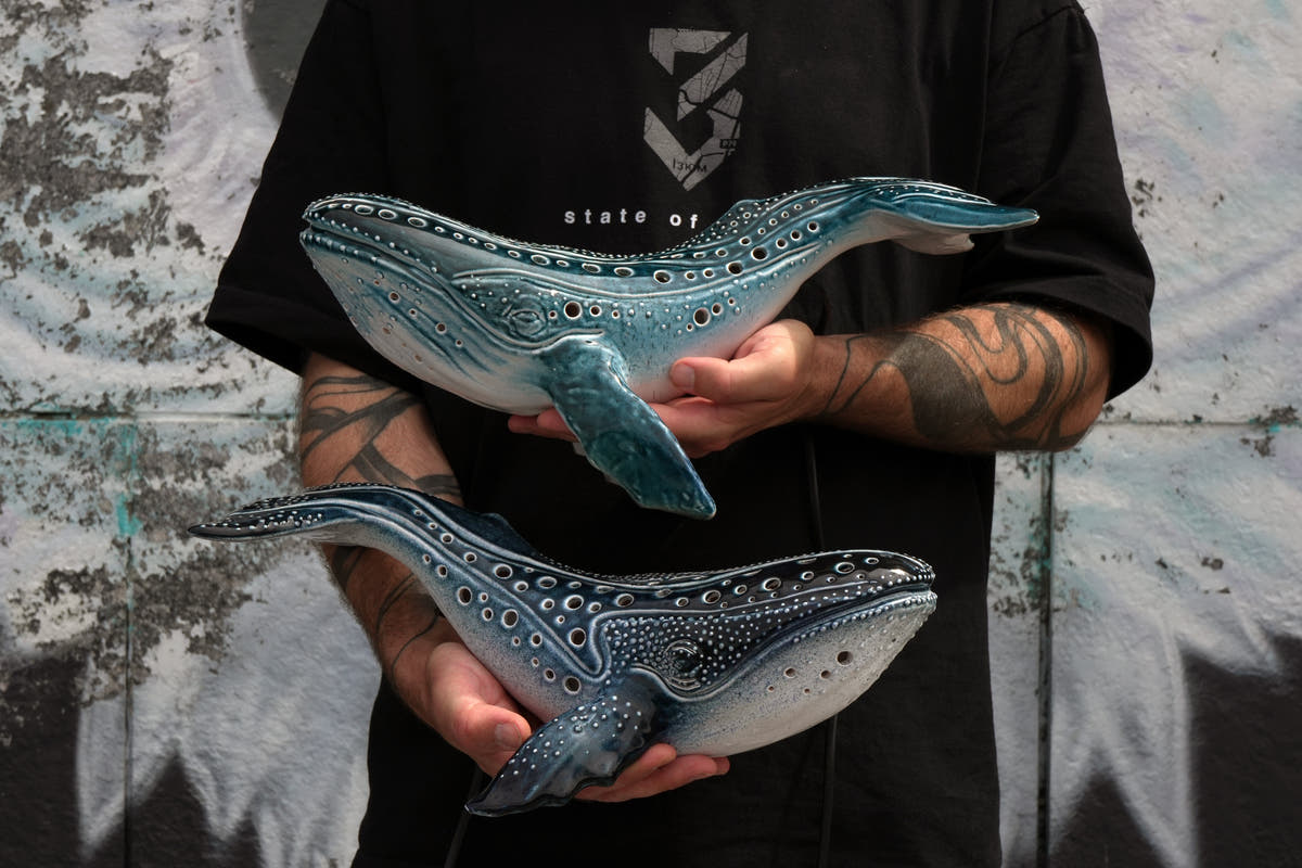 Viktor Kushchenko is holding ceramic whale lamps in front of the wall with graffiti 