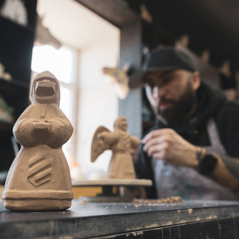 Man working on a sculpture in a workshop with clay figures.
