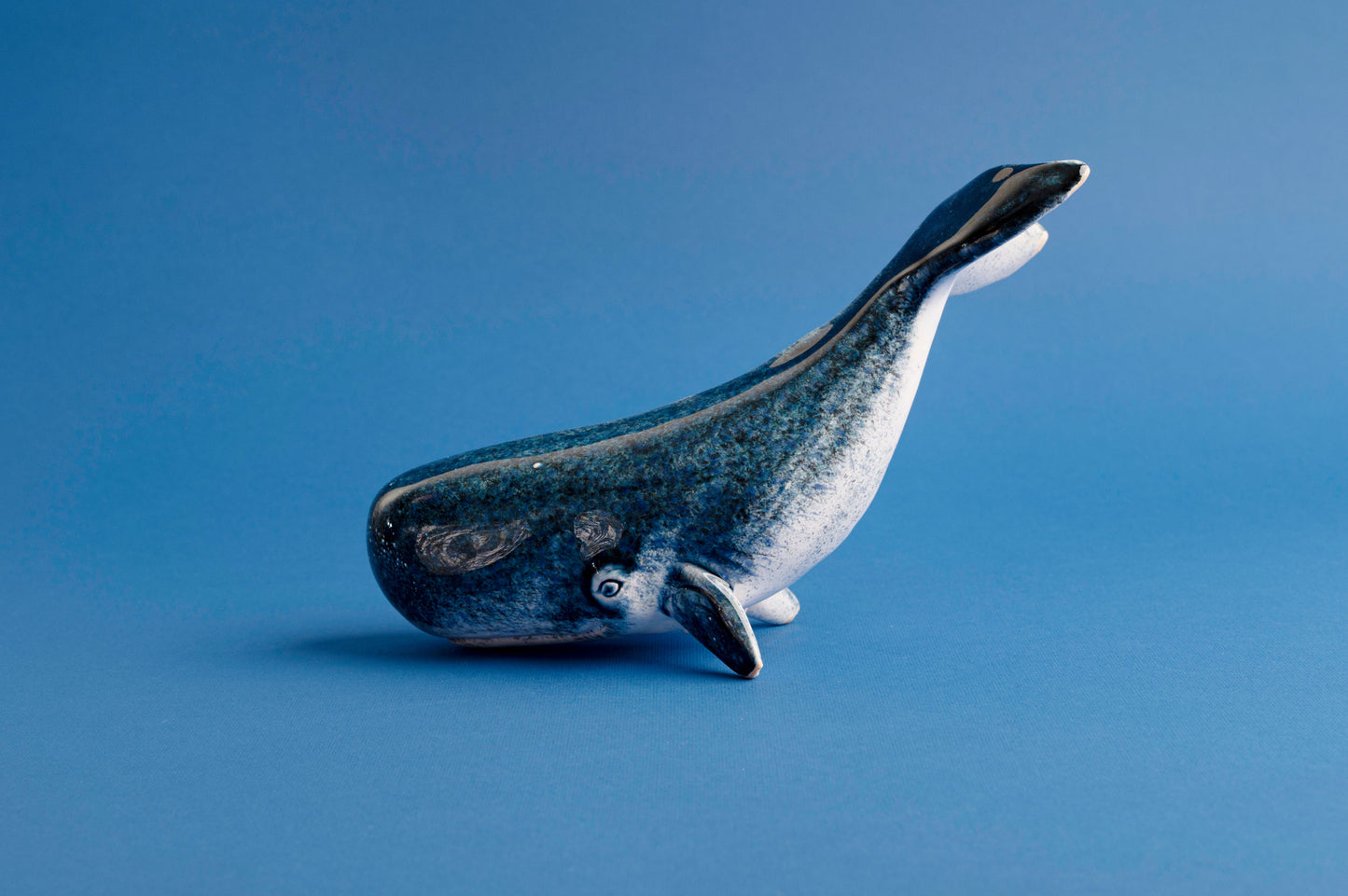 Blue ceramic whale figurine on a blue background