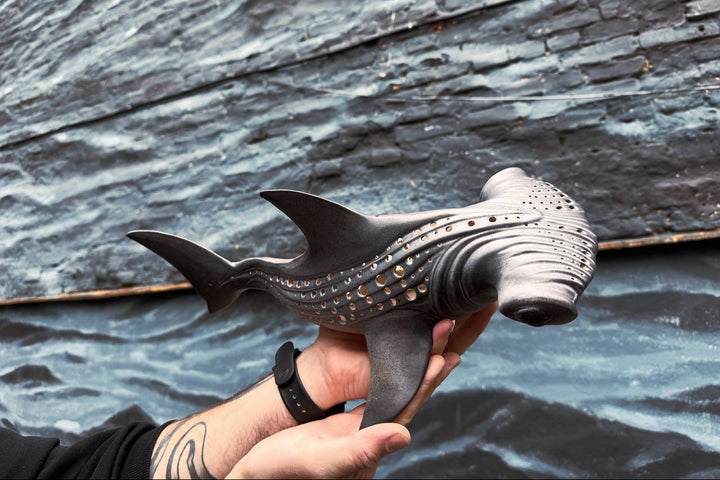 Hand holding a shark-shaped object against a ocean background