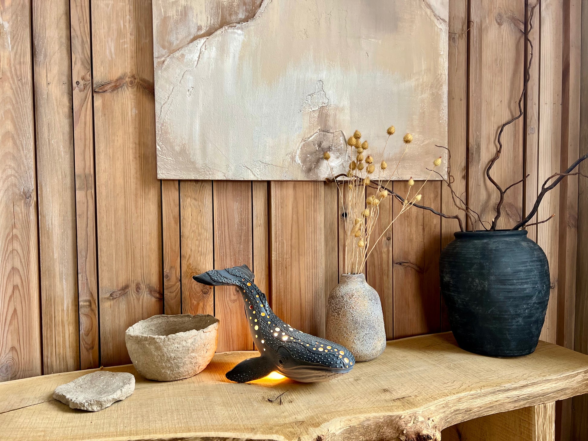 Decorative setting with vases, a bowl, and a whale sculpture on a wooden surface against a wooden wall.