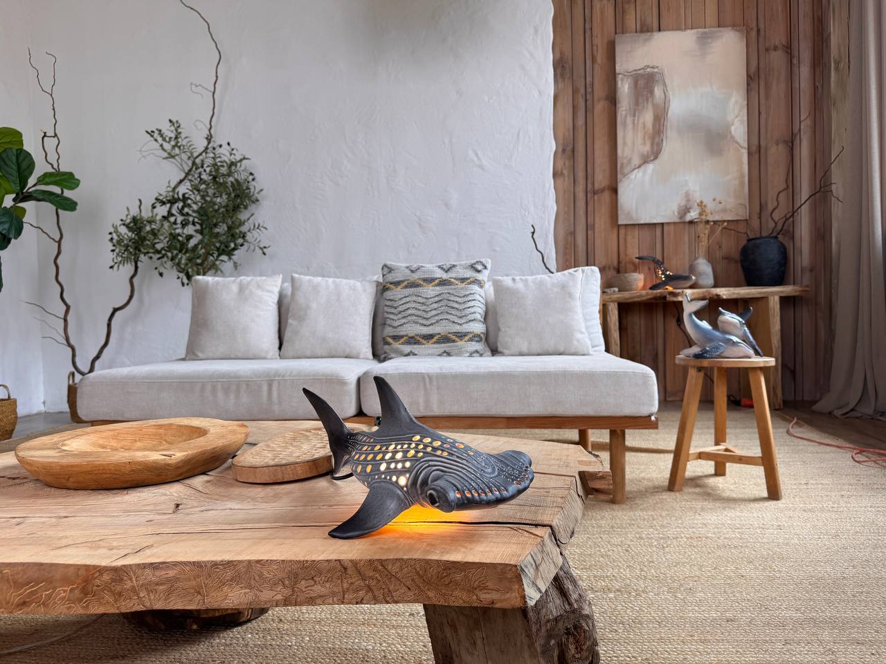 Living room with a shark sculpture on a wooden coffee table, plants, and a sofa.