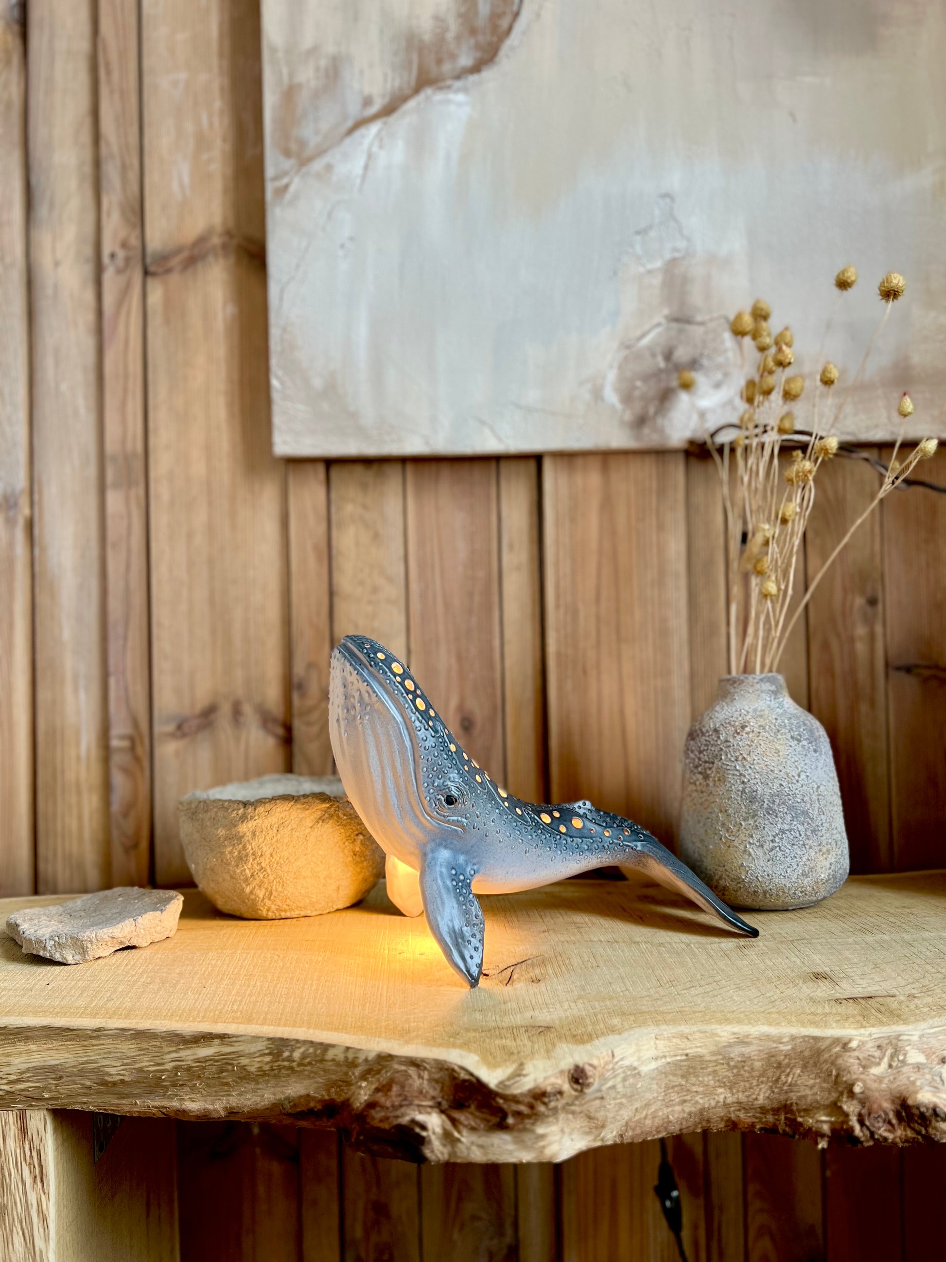 Decorative whale sculpture on a wooden surface with a vase and stones in the background.