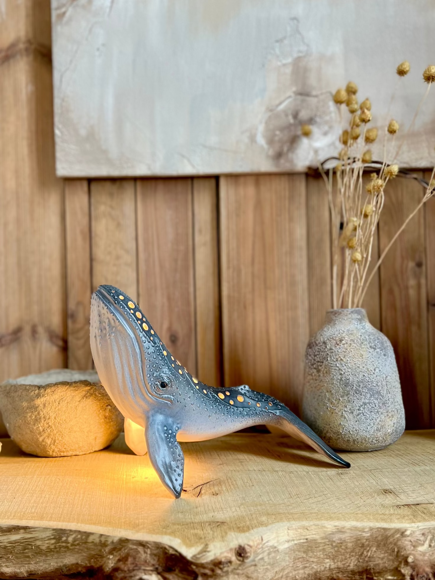 Decorative whale sculpture on a wooden surface with a vase and stones in the background.