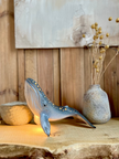 Decorative whale sculpture on a wooden surface with a vase and stones in the background.