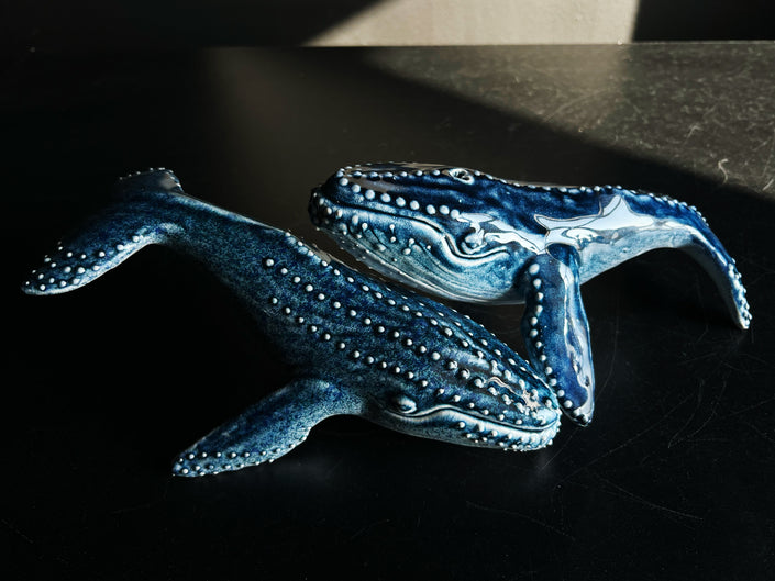 Two blue whale sculptures on a dark surface