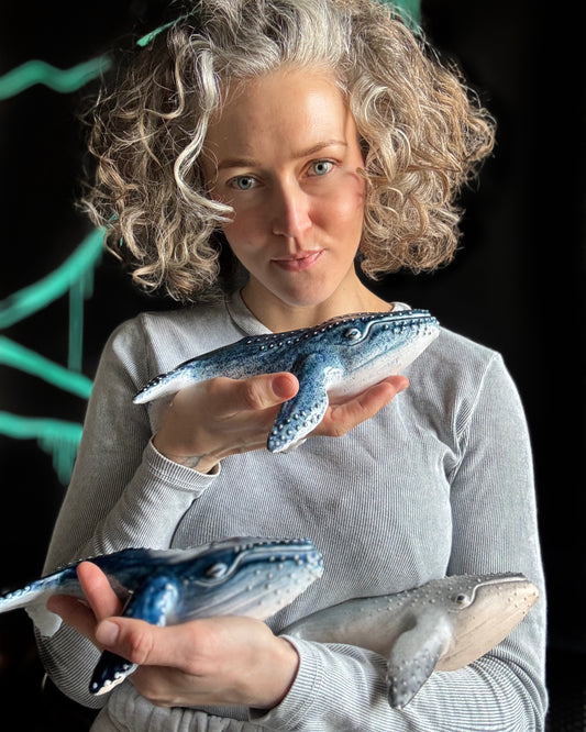 Woman holding three whale figurines against a dark background