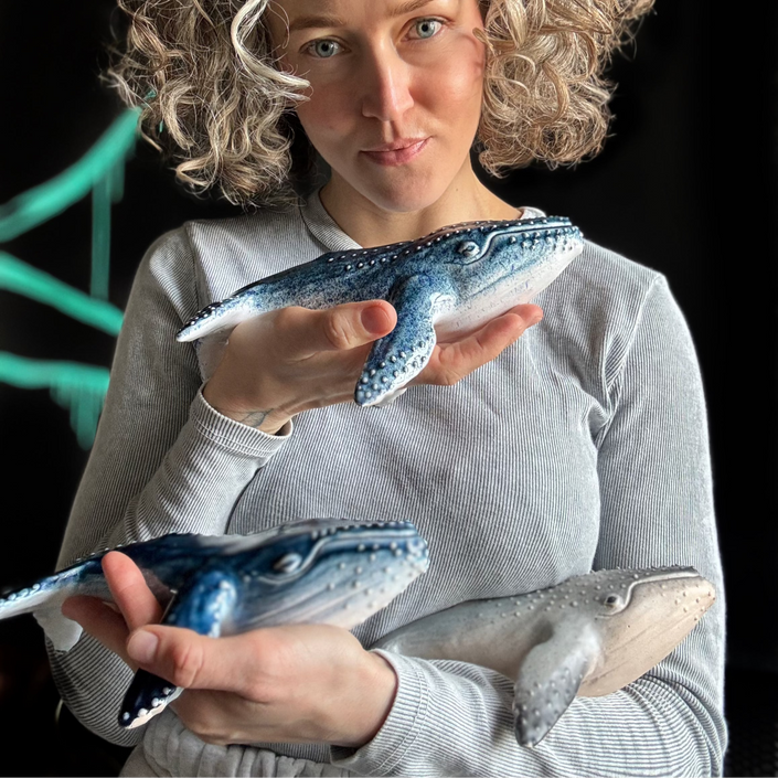 Woman holding three whale figurines against a dark background