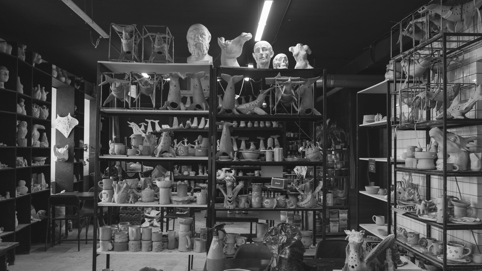 Black and white photograph of a pottery studio with shelves filled with ceramic items.