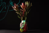 Decorative vase with colorful leaf design containing red and green leaves on a black background
