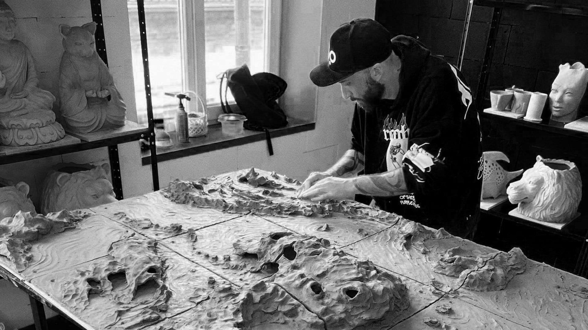 Person working on a sculpture of a mountainous landscape in a workshop.