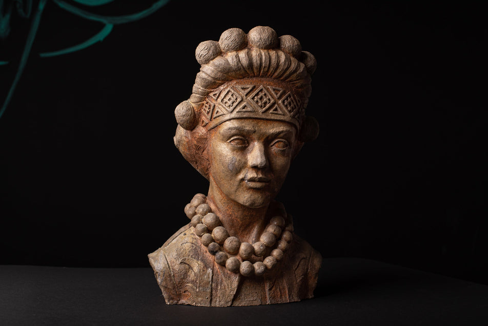 Ceramic bust of a figure with intricate headpiece and necklace on a dark background