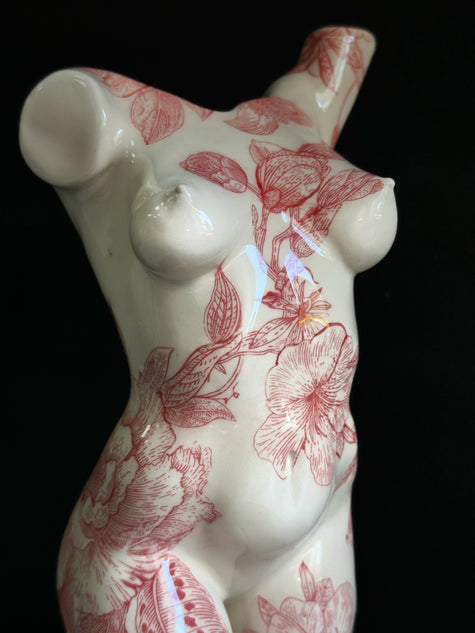 Ceramic sculpture of a female torso with red floral patterns on a black background