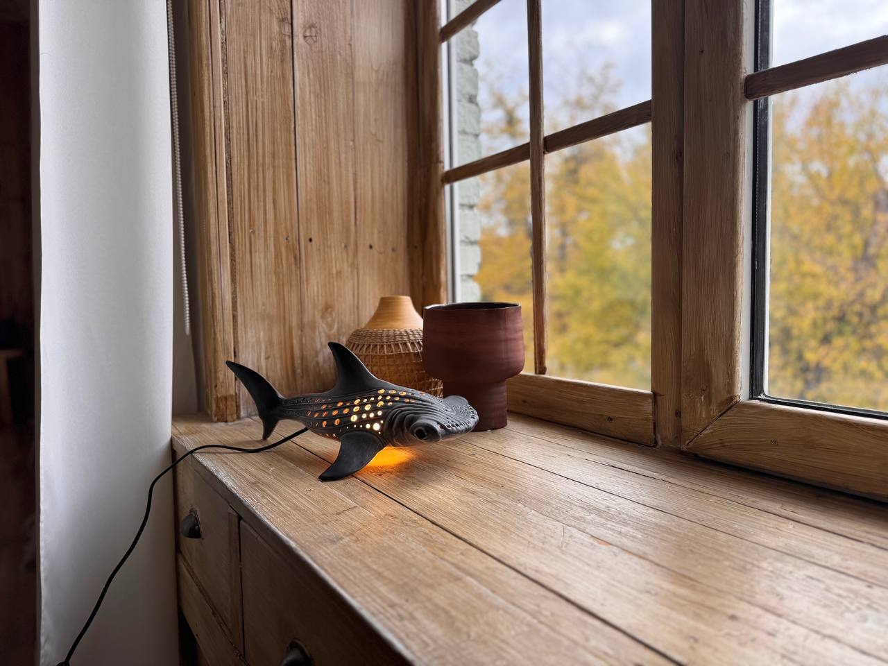 Decorative lamp shaped like a fish on a wooden surface with a window in the background