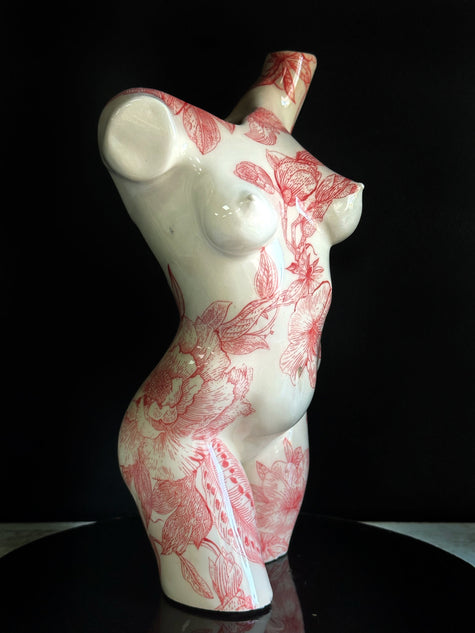 Ceramic sculpture of a female torso with red floral patterns on a black background
